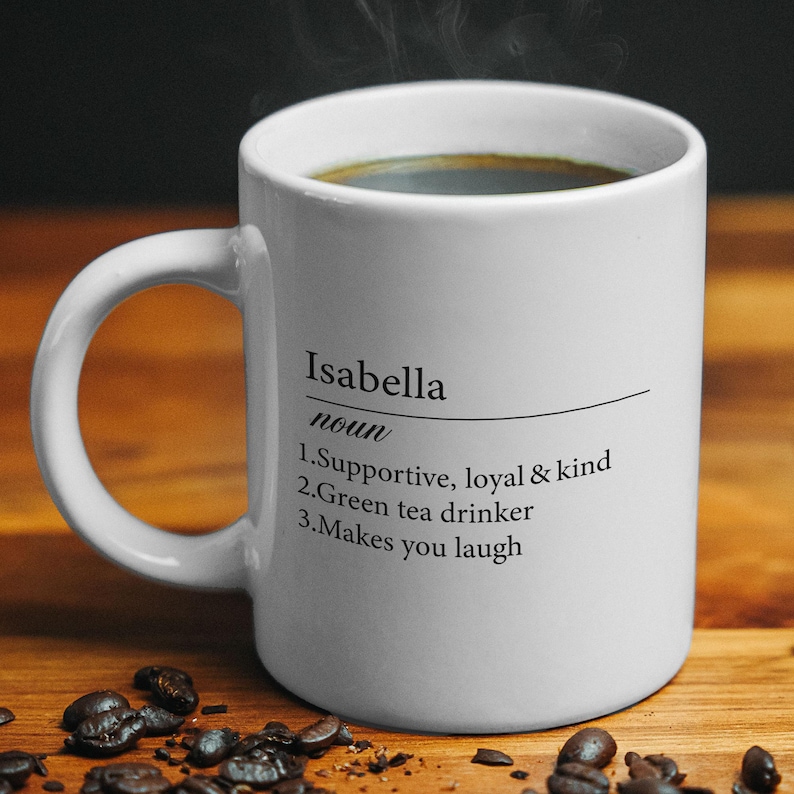 May include: White ceramic coffee mug with a black inscription that reads "Isabella noun 1. Supportive, loyal & kind 2. Green tea drinker 3. Makes you laugh"