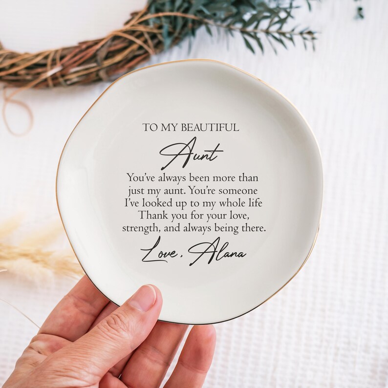 May include: White ceramic trinket dish with a gold rim. The dish has a message that reads "To my beautiful Aunt You've always been more than just my aunt. You're someone I've looked up to my whole life. Thank you for your love, strength, and always being there. Love, Alana"