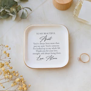 May include: White ceramic trinket dish with a gold rim. The dish has a message that reads "To my beautiful Aunt You've always been more than just my aunt. You're someone I've looked up to my whole life. Thank you for your love, strength, and always being there. Love, Alana."