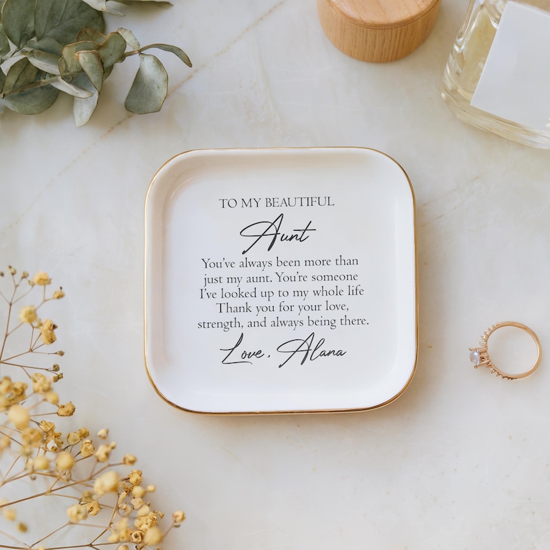 May include: White ceramic trinket dish with a gold rim. The dish has a message that reads "To my beautiful Aunt You've always been more than just my aunt. You're someone I've looked up to my whole life. Thank you for your love, strength, and always being there. Love, Alana."