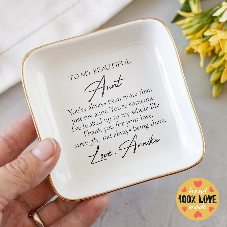 May include: White ceramic trinket dish with a gold rim. The dish has a message that reads "To my beautiful Aunt You've always been more than just my aunt. You're someone I've looked up to my whole life Thank you for your love, strength, and always being there. Love, Annika".