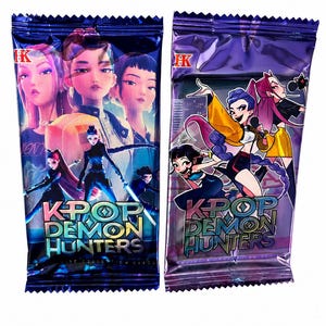 May include: Two sealed trading card packs. The packs are dark blue and purple with the text "K-POP DEMON HUNTERS". The front of the packs feature anime-style illustrations of female characters in vibrant colors.
