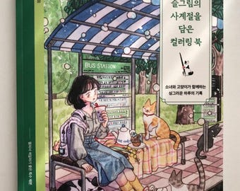May include: A coloring book with a cover illustration of a girl at a bus stop with cats. The book's title is in Korean. The girl is drinking a beverage and the bus stop has a blue and white striped roof. The book is green and white.