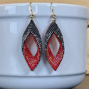 Pode incluir: Um par de brincos pendentes com um design em forma de marquise feito de pequenas contas. A parte superior é cinzento-escura, passando para uma secção inferior vermelha vibrante com um centro aberto. Ganchos de tom dourado.