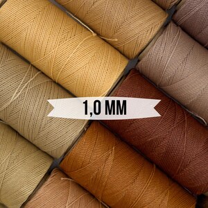 Könnte beinhalten: Spulen mit gewachstem Garn in verschiedenen Brauntönen, Beige und Braun. Die Spulen sind kreisförmig angeordnet mit dem Text "1,0 MM" in der Mitte.