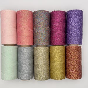 Peut inclure: Dix bobines de fil coloré et brillant. Le fil est disposé en rangée, chaque bobine étant d'une couleur différente. Les couleurs sont rose, corail, multicolore, magenta, violet, vert clair, argent, or, marron et rouge.