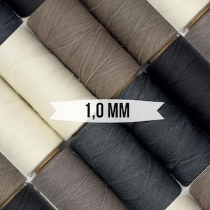 Puede incluir: Primer plano de carretes de hilo encerado en varios colores, incluyendo negro, marrón, beige y blanco. Los carretes están dispuestos en un patrón y el texto "1,0 MM" es visible en el centro de la imagen.