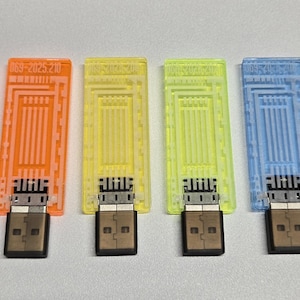 May include: A collection of six USB flash drives in various colors: red, orange, yellow, green, blue, and purple. Each drive has a rectangular, translucent top with a circuit board design and a USB connector.