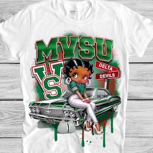 May include: White t-shirt featuring the text "MVSU" in green and red, with a cartoon character sitting on a green classic car. The shirt also includes the words "Delta Devils".