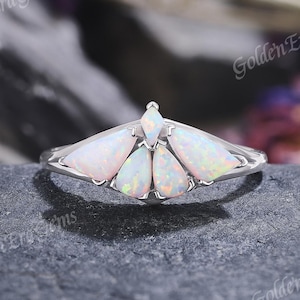 May include: A silver-toned ring featuring five pear-shaped, iridescent white opals arranged in a fan-like pattern. The central opal is topped with a small, diamond-shaped opal, creating a symmetrical design set on a polished metal band.
