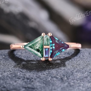 May include: A rose gold ring featuring a kite-shaped moss agate on the left, a kite-shaped alexandrite on the right, and a small rectangular alexandrite baguette set vertically in the center between the two larger stones.