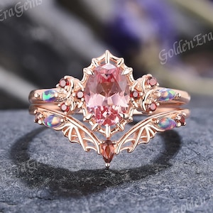 Könnte beinhalten: Ein Verlobungsring aus Roségold mit einem filigranen, komplizierten Design. Der mittlere Stein ist ein großer ovaler rosa Edelstein, der von kleineren Edelsteinen umgeben ist. Der Ring ist mit einem filigranen, komplizierten Design verziert.