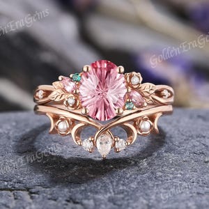 May include: A rose gold engagement ring set with a large oval pink gemstone as the centerpiece. The ring is adorned with smaller pink and green gemstones, pearls, and diamonds. The band features a delicate, ornate design.