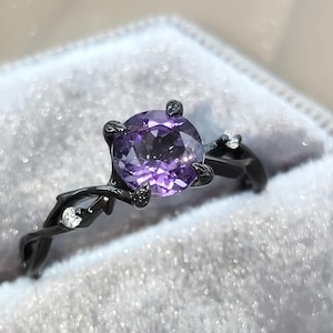 May include: A black ring with a purple gemstone set in a twisted vine design. The ring is in a black velvet ring box.