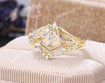 May include: A gold ring featuring a fan-shaped arrangement of clear, trapezoidal stones and a marquise-cut stone at the top. The band is accented with a V-shaped row of marquise and round-cut stones. The text GoldenEraGems is visible.