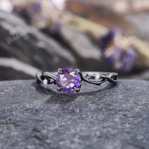 May include: Black gold ring with a purple amethyst gemstone and small white diamonds set in a vine design.