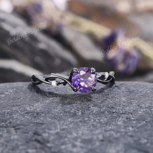 May include: A black gold ring with a purple amethyst gemstone and small white diamonds set in a vine-like design.