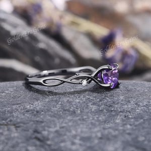 May include: Black gold ring with a purple heart-shaped amethyst gemstone and small diamond accents. The ring band is a delicate, twisted vine design.