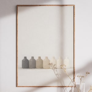 Puede incluir: Impresión enmarcada que presenta seis pequeñas botellas redondeadas en tonos grises y beige. Las botellas están dispuestas sobre una superficie blanca sobre un fondo blanco. El marco es de color marrón claro.