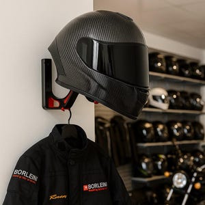 May include: A black motorcycle helmet with a carbon fiber weave pattern is mounted on a wall. The helmet has a dark visor and is displayed with a black jacket that has the text "BORLEINI" and "Racing Gloves" on it. Other helmets are visible in the background.