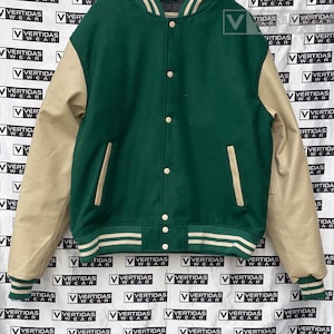 May include: A green and tan varsity jacket with a white stripe on the collar and cuffs. The jacket has a button closure and a pocket on the left side.