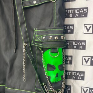 May include: Black pants with green stitching and a skull patch. The pants have multiple straps and buckles. The pants are labeled "VERTIDAS WEAR".