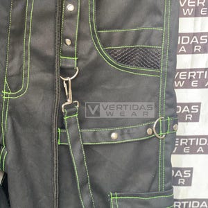 May include: Black pants with green stitching and a mesh pocket. The pants have a zipper fly and a belt loop. The pants have a large pocket on the right leg with silver studs.