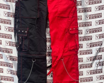 Op de afbeelding: Zwarte en rode gesplitste cargobroek met rode stiksels en zilveren kettingaccenten. Voorzien van meerdere zakken, metalen ringen en stud details. De broek heeft een taille met trekkoord en is gemaakt van een duurzame stof.