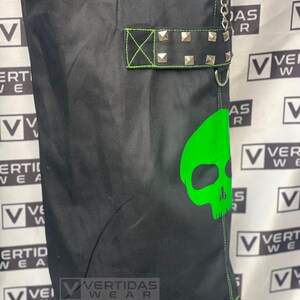May include: Black cargo pants with a green skull graphic and a black belt with silver studs. The pants have a green drawstring and the text "VERTIDAS WEAR" is visible on the pants.