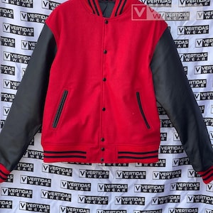 Puede incluir: Una chaqueta de béisbol roja y negra con una manga de cuero negro. La chaqueta tiene cierre de presión y cuello, puños y cintura de canalé.