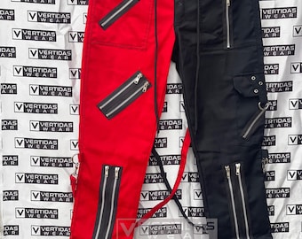Op de afbeelding: Zwarte en rode broek met ritsdetails en een contrasterende kleurscheiding langs de middelste naad. De broek heeft meerdere ritszakken en een riemlus.