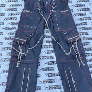 May include: Black cargo pants with red stitching and silver chain accents. Features multiple pockets, zippers, and metal hardware. The pants have a unique, edgy design.