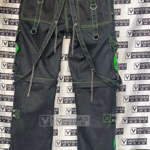 May include: Black pants with green stitching and silver chains. The pants have multiple pockets and a mesh panel on the back. The pants are labeled "Vertidas Wear".