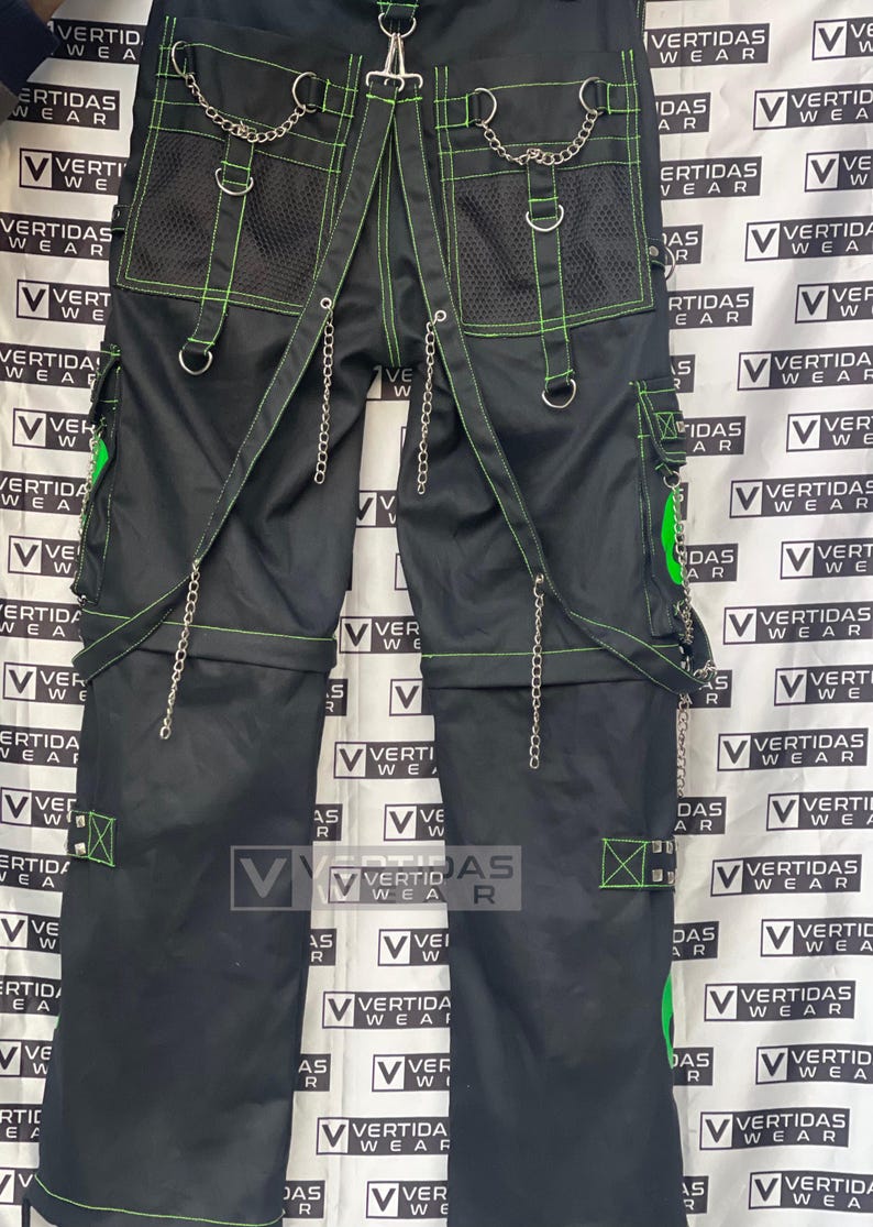 May include: Black pants with green stitching and silver chains. The pants have multiple pockets and a mesh panel on the back. The pants are labeled "Vertidas Wear".