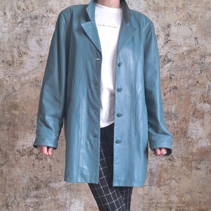 May include: A teal leather jacket with a classic lapel collar and button closure. The jacket is worn over a white t-shirt and black and white checkered pants. The jacket has long sleeves and a tailored fit.