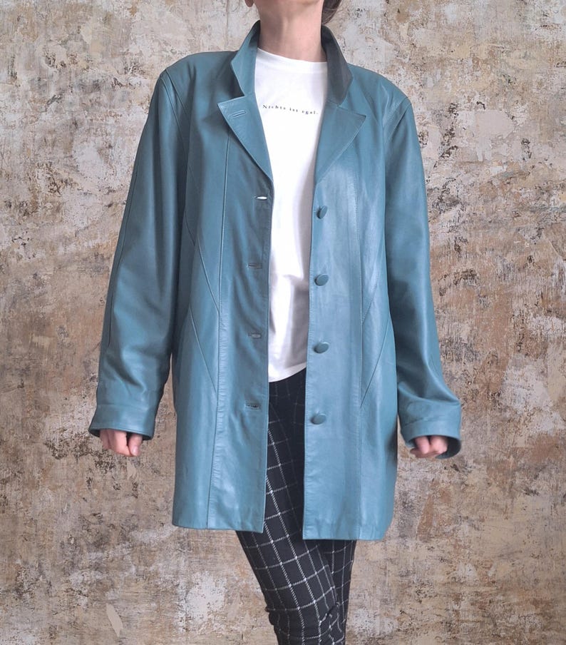 May include: A teal leather jacket with a classic lapel collar and button closure. The jacket is worn over a white t-shirt and black and white checkered pants. The jacket has long sleeves and a tailored fit.