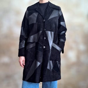 Peut inclure: Manteau noir en patchwork avec un col, une fermeture boutonnée et deux poches avant. Le manteau présente un mélange de panneaux en daim et en cuir cousus ensemble. Le manteau arrive au genou et est porté avec un jean bleu.