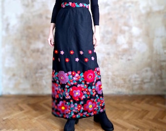Puede incluir: Una falda larga negra con un diseño bordado floral. La falda presenta una variedad de colores, incluyendo rojo, rosa, verde y amarillo. El bordado es detallado e intrincado.