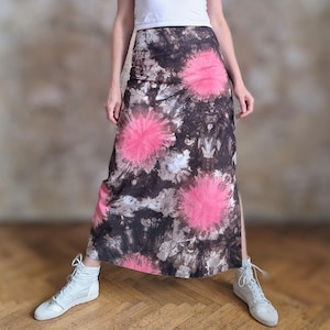 Könnte beinhalten: Ein langer Batikrock mit hohem Schlitz, der große rosa kreisförmige Muster auf einem braunen und grauen Hintergrund aufweist. Der Rock wird mit einem weißen Oberteil und weißen Turnschuhen kombiniert.