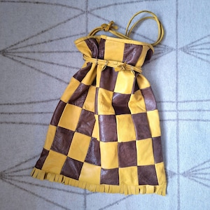 Peut inclure: Un sac à cordon fait à la main avec un motif en damier. Le sac est fait de carrés de cuir marron et jaune. Le haut a une fermeture à cordon et une lanière en cuir. Le bord inférieur a une frange.