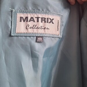 May include: Close-up of the inside of a light blue leather jacket. A label reads "MATRIX Collection GERMANY" with the size "48" below it. The jacket's lining is a matching light blue color.