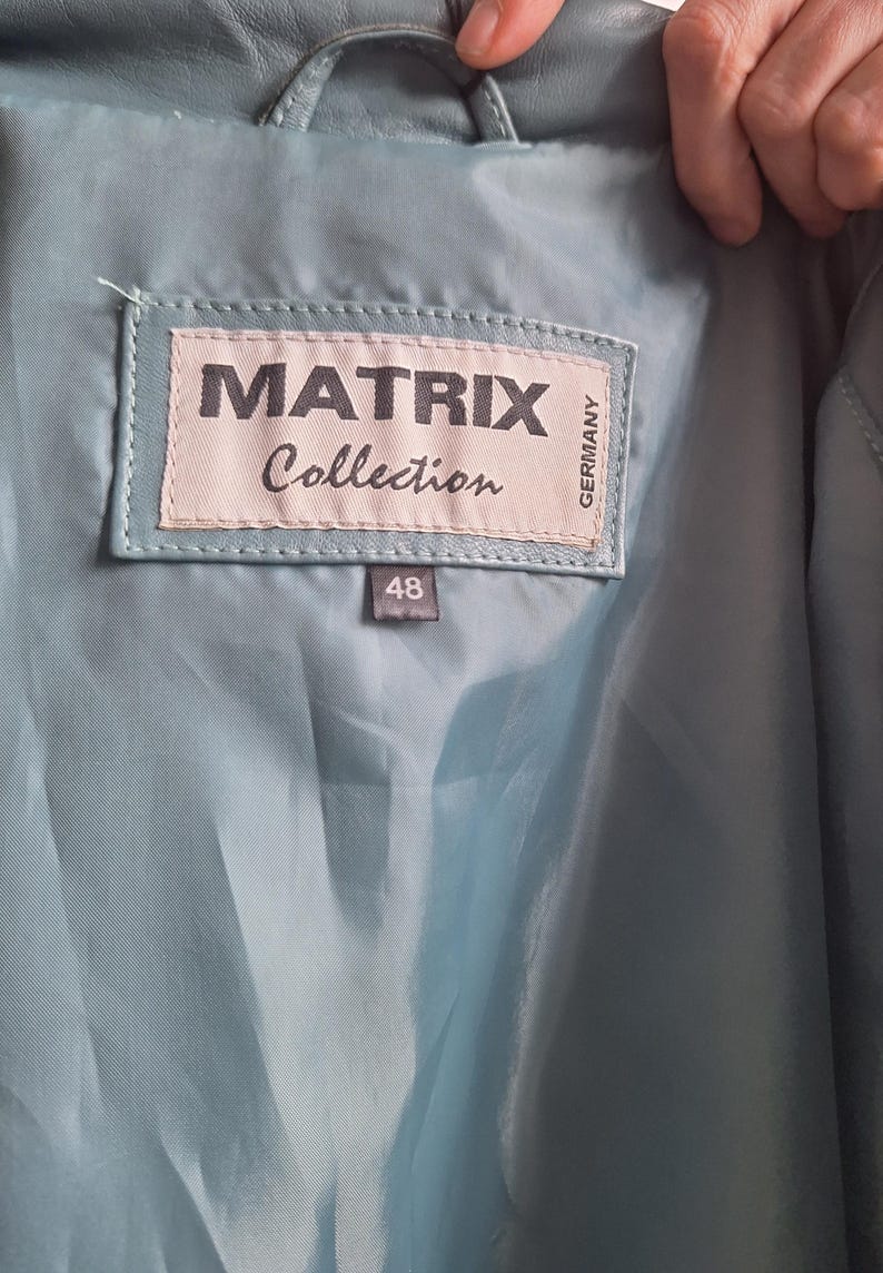 May include: Close-up of the inside of a light blue leather jacket. A label reads "MATRIX Collection GERMANY" with the size "48" below it. The jacket's lining is a matching light blue color.