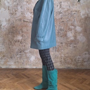 May include: A teal leather blazer with a double-breasted design. The blazer is paired with black and white checkered leggings and teal suede boots. The boots reach the knees.