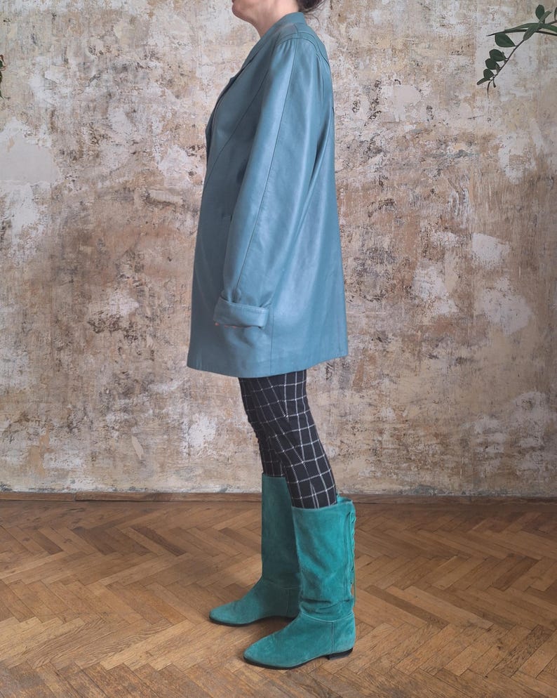 May include: A teal leather blazer with a double-breasted design. The blazer is paired with black and white checkered leggings and teal suede boots. The boots reach the knees.