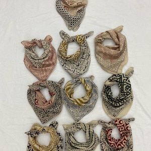 May include: Nine cotton bandanas with different patterns in shades of red, brown, blue, green, and yellow. The bandanas are tied in a knot and arranged in a triangular pattern on a white background.