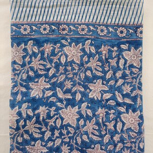 K&ouml;nnte beinhalten: Ein blauer Baumwollstoff mit einem wei&szlig;en Blumenmuster. Der Stoff hat einen wei&szlig;en und blauen gestreiften Rand.