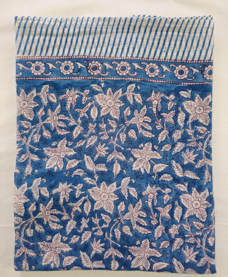 K&ouml;nnte beinhalten: Ein blauer Baumwollstoff mit einem wei&szlig;en Blumenmuster. Der Stoff hat einen wei&szlig;en und blauen gestreiften Rand.