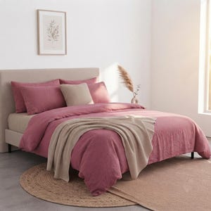 May include: A bed featuring a dusty rose duvet cover and matching pillowcases, complemented by a beige throw blanket and a single beige square throw pillow. The bed has a tall, upholstered headboard in a neutral light beige fabric.