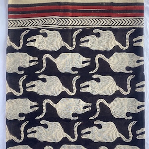 May include: A textile with a repeating pattern of stylized tigers in cream against a dark navy background. The top border features a cream band with red stripes and a chevron design. The fabric appears to be handmade.
