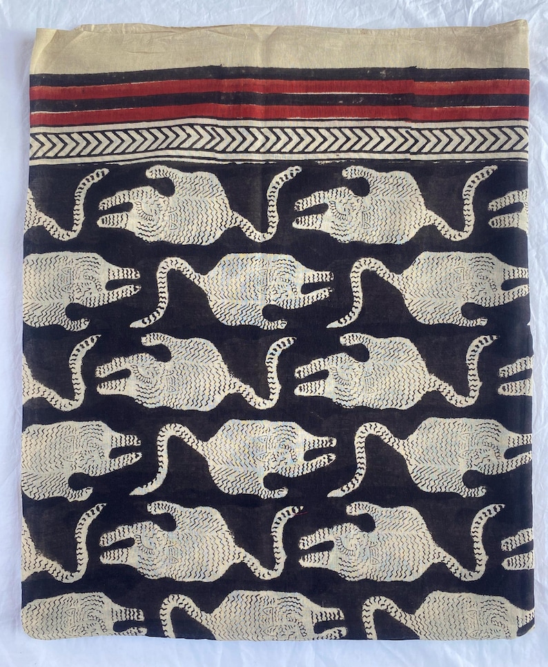 May include: A textile with a repeating pattern of stylized tigers in cream against a dark navy background. The top border features a cream band with red stripes and a chevron design. The fabric appears to be handmade.